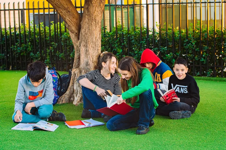 Primary pupils reading together on the grass under a tree